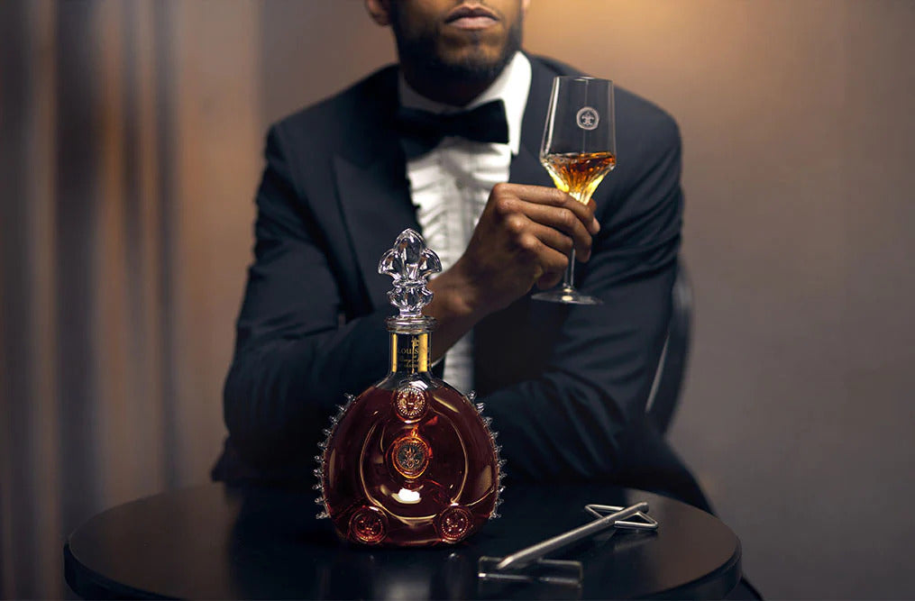 A lifestyle photo of a well dressed man touching LOUIS XIII decanter on the table, a bar in the background