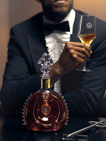 A dimme dimage of a man watching a bartender serving LOUIS XIII to a cristal glass using a spear