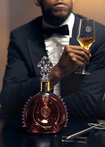 A dimme dimage of a man watching a bartender serving LOUIS XIII to a cristal glass using a spear