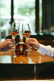 A lifestyle image of two hands toasting with LOUIS XIII cristal glasses, a decanter in the background