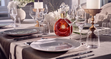 Bottle of Louis XIII cognac placed at the center of a festive arrangement with candles, flowers, plates and crystal glasses.