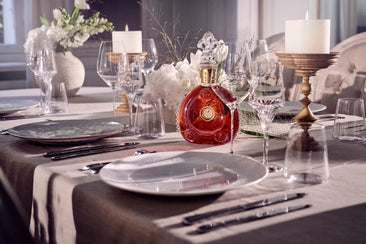 Bottle of Louis XIII cognac placed at the center of a festive arrangement with candles, flowers, plates and crystal glasses.