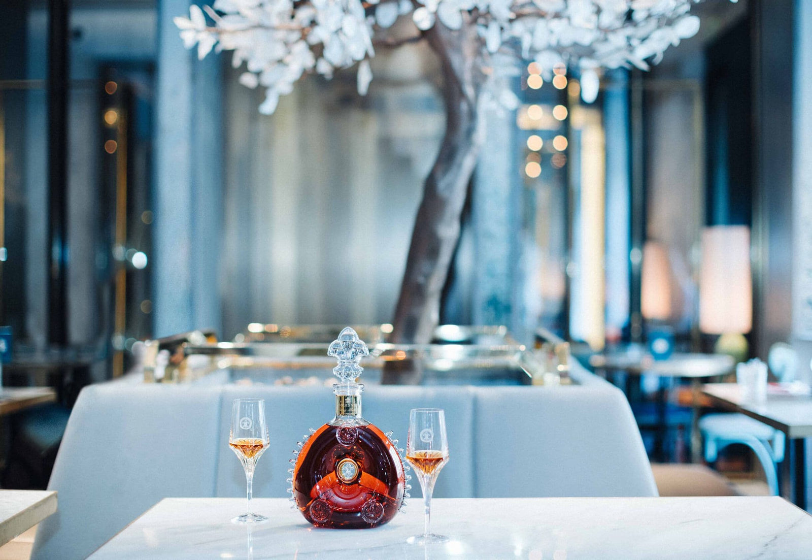 A lifestyle photo of a LOUIS XIII decanter on a restaurant table, two crystal engraved glasses on both sides