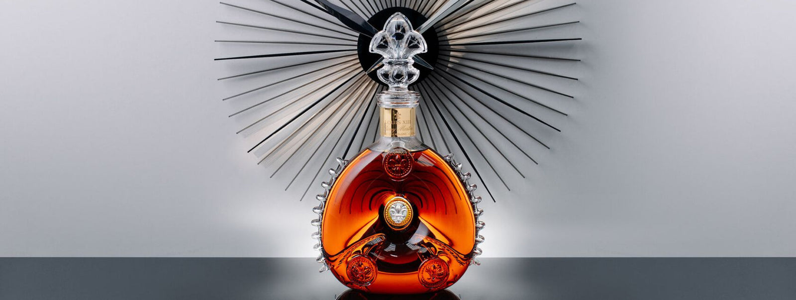 A lifestyle photo of LOUIS XIII decanter on a black surface, black modern clock behind