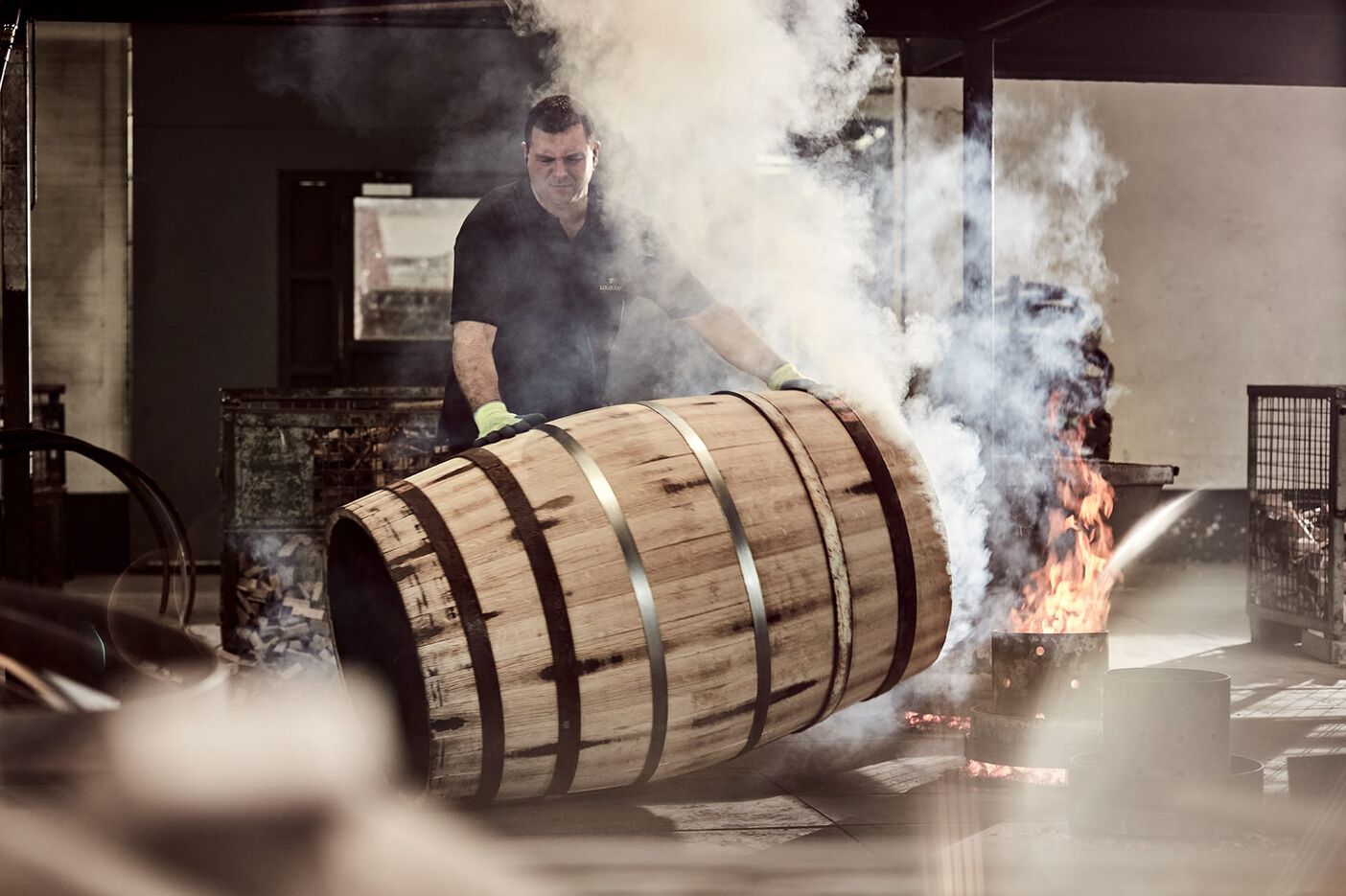 A photo of a man in black tshirt preparing a new LOUIS XIII barrel, fire and smoke